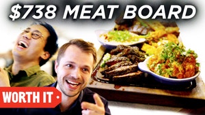 Steven and Andrew laugh next to a picture of a giant meatboard with lots of meat and side dishes. 