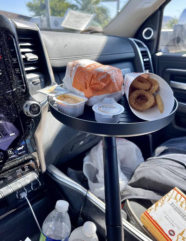 Fast food meal including sandwiches, onion rings, and sauces on a car tray inside a vehicle