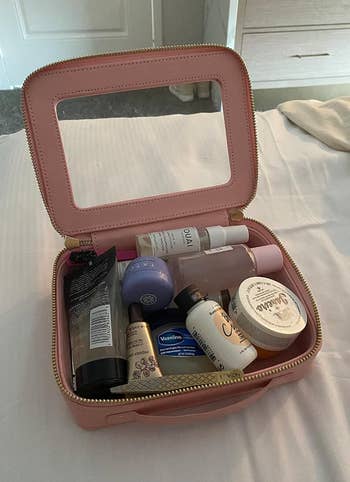 Open pink cosmetic bag with various skincare and beauty products, including items from brands Ouai, Tatcha, Vaseline, and Dr. Bronner's