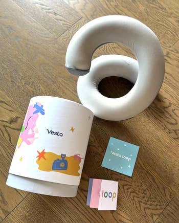 Neck pillow with Vesta branding, packaging, and booklets on a wooden surface