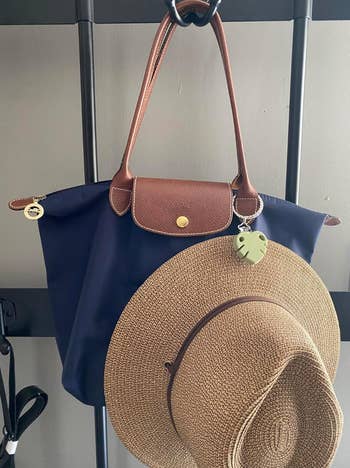 A woven hat and a stylish tote bag hang on a rack; a leaf-shaped charm is attached to the bag