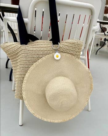 Straw bag with a wide-brimmed straw hat and daisy keychain, hanging on a white chair. Perfect for a beach day shopping look