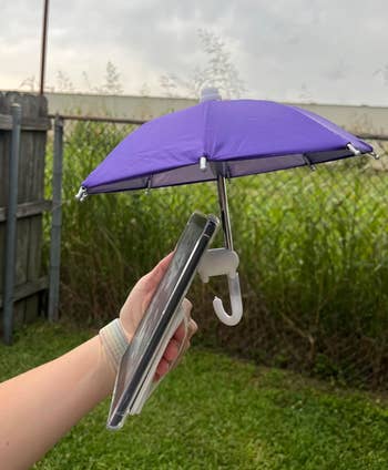 A hand holding a phone with a small umbrella attachment to shield it from rain