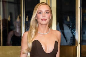 A woman with long, wavy hair in an elegant, strapless gown poses at an event entrance, accessorized with a necklace