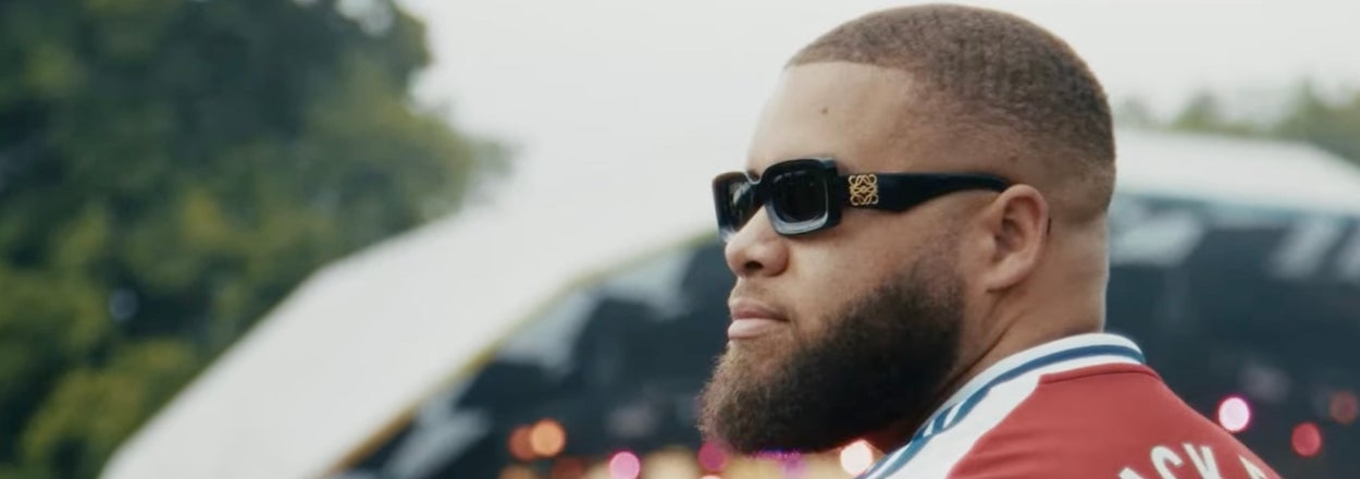 A person with sunglasses and a beard looks towards an outdoor stage, wearing a jersey with "Black 3" on the back