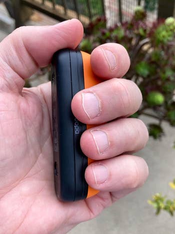 Person holding a compact electronic device with an orange and black design