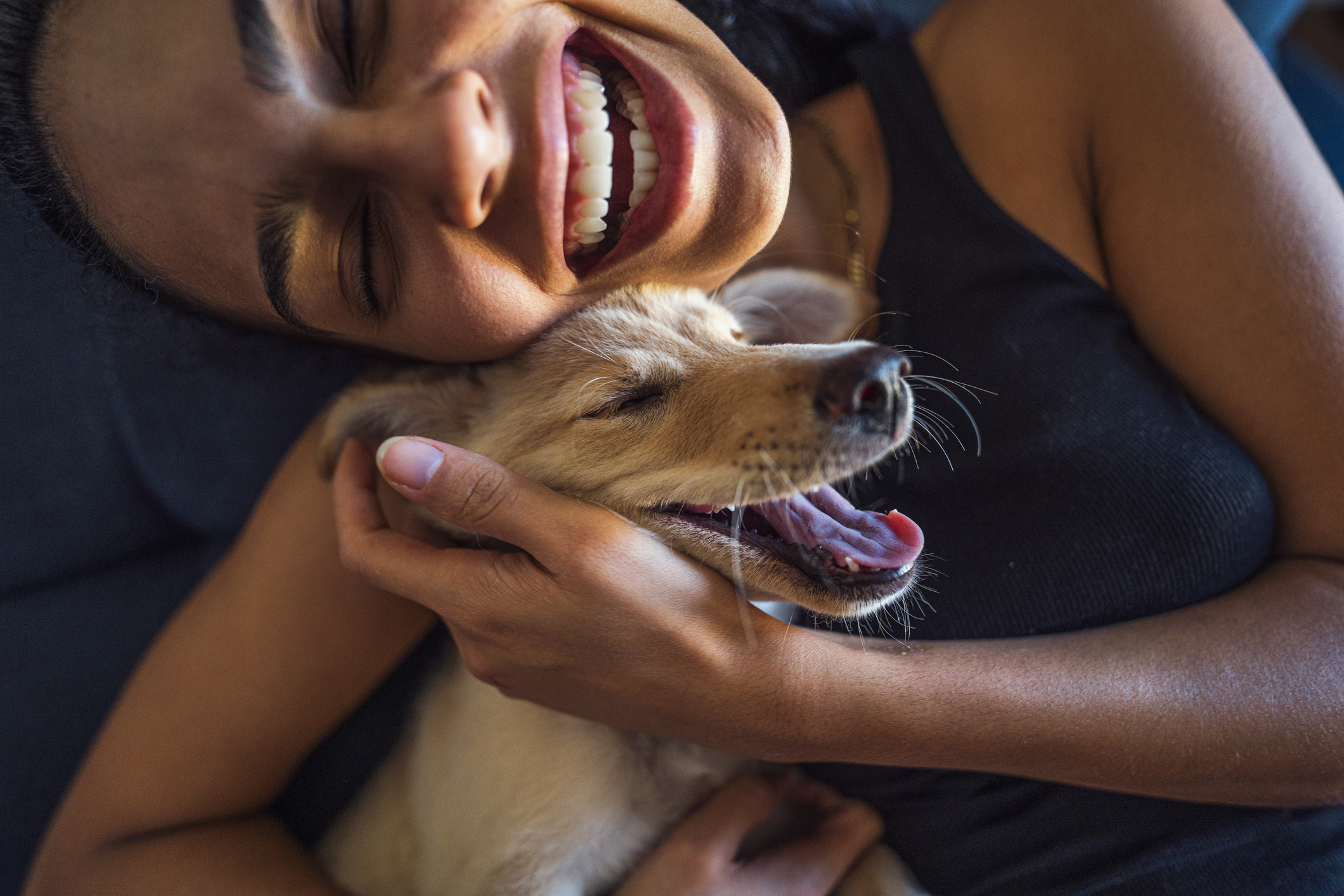 Smiling person cuddles a happy puppy, both with eyes closed, enjoying a joyful moment