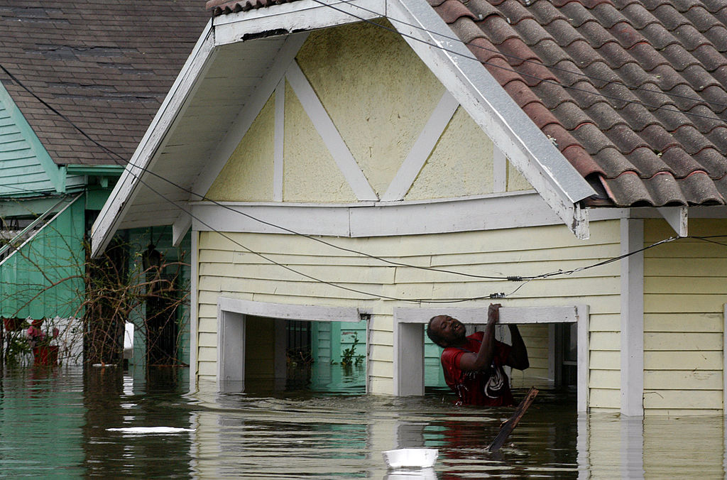 A person climbs out of a flooded house&#x27;s window, surrounded by rising water, during a natural disaster scene