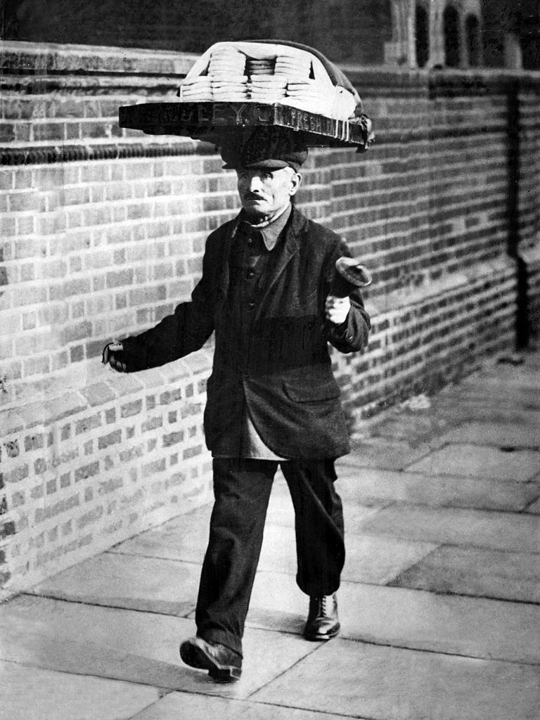 A man walking on the street with a large tray with pastries on it