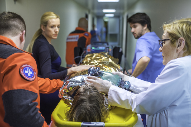 Medical team in a hospital hallway, working urgently on a patient covered with a thermal blanket on a stretcher