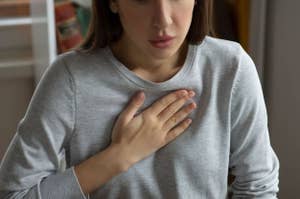 Woman touching her chest with one hand, appearing concerned, wearing a long-sleeved, casual top. No visible colors or text in the image