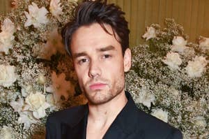 Liam Payne in a dark suit stands in front of flower arrangements