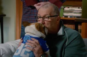 Man kissing a dog wearing jersey; books in background