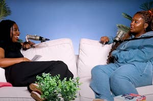 Two women sit on a white couch, having a lively conversation on a podcast, with microphones in front of them