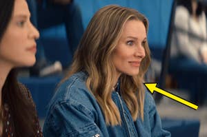 Kristen Bell seated indoors on gym bleachers with a shocked expression in a scene from "Nobody Wants This"