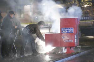 People inspect a smoking ballot drop box with police nearby