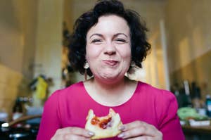 Person smiling while holding and eating a pastry in a kitchen setting