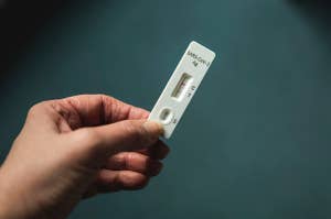 Hand holding a COVID-19 rapid test showing a positive result with lines at both "C" and "T" indicators