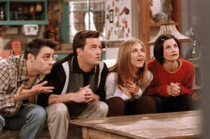 Joey Tribbiani, Chandler Bing, Rachel Green, and Monica Geller are sitting on a cozy couch, intently watching something off-camera