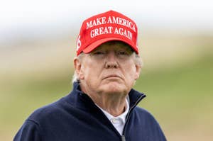 Donald Trump wearing a "Make America Great Again" cap and a dark zip-up jacket, standing outdoors