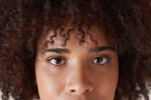 Close-up of a person's face with curly hair, focusing on their eyes and skin texture.