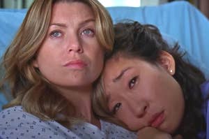 Ellen Pompeo and Sandra Oh are sitting closely. Pompeo appears pensive while Oh rests her head on Pompeo's shoulder, giving a comforting and intimate vibe