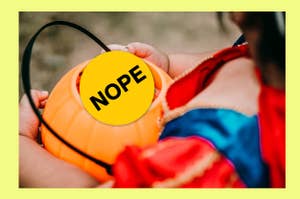 Child in costume holding an empty Halloween candy bucket with a "NOPE" sign on it.