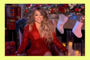 Mariah Carey wearing a sparkly red dress, sitting in front of a festive background with stockings and candles