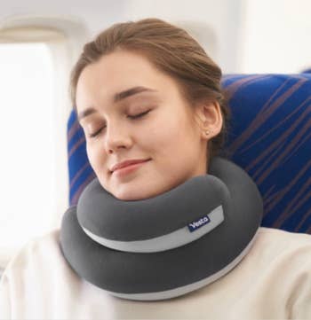 Person sleeping in an airplane seat using a Vedta neck pillow for support